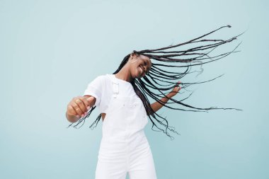 Beyaz giysili mutlu kadın dans ederken uzun örgülü saçlarıyla uçuyor.