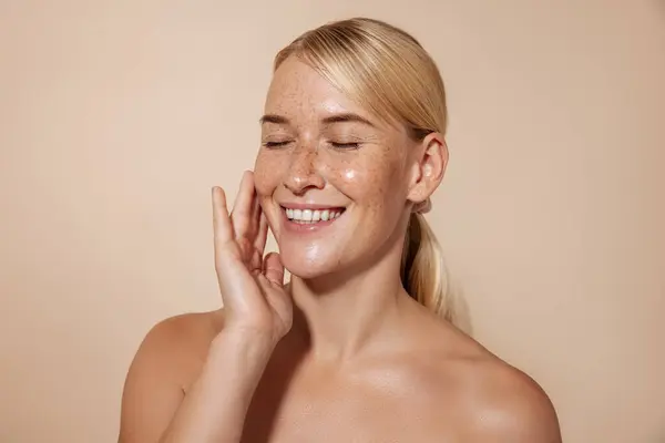 Stüdyoda sarı saçlı mutlu kadın yüzüne dokunuyor. 