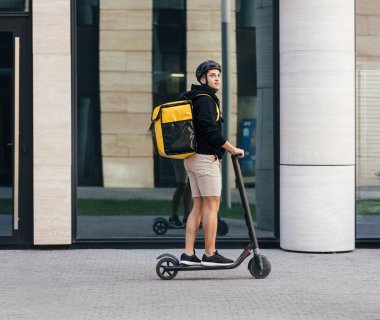 Erkek kuryenin elektrikli scooter 'a binerken yandan görünüşü ve yemek paketi.