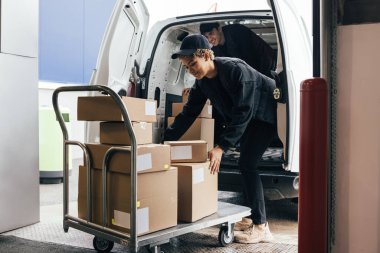 Dişi kurye, bir meslektaşı içinde dururken karton kutuları bir arabaya yüklüyor.