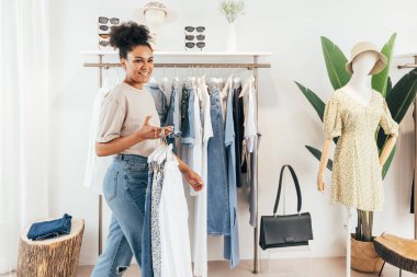 Küçük bir moda mağazasında çalışan bir kadın. Elinde bir sürü elbise askısı olan bir kadın.