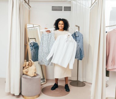 Soyunma odasında askılarıyla kameraya bakan şık bir kadın.