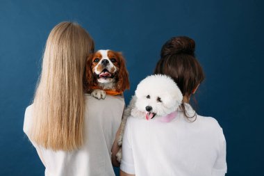 Köpekleriyle ayakta duran iki kadının arka görüntüsü. Omzunda yatan iki küçük köpeğin portresi.