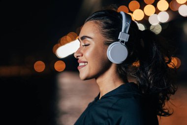 Gece lambalarının karşısında duran kulaklıklı, gülümseyen kadına yaklaş.