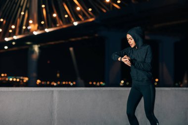 Genç sporcu kadın gece dışarıda koşarken akıllı saatlere bakıyor.
