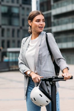 Şehirde elektrikli scooterıyla gezen neşeli iş kadını.