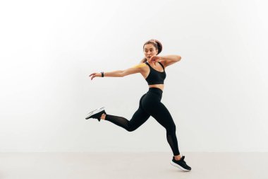 Asyalı kadın beyaz bir duvara doğru atlayıp koşarken arkasına bakıyor.