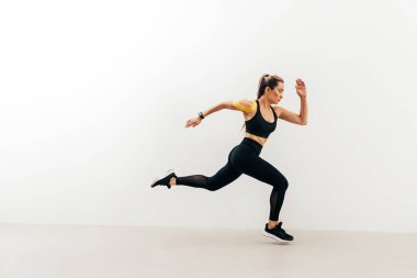 Beyaz bir duvarın yanında koşan bayan sporcunun yan görüntüsü