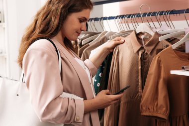 Zarif bir kadının elbise askısı tutarken akıllı telefona bakışının yan görüntüsü