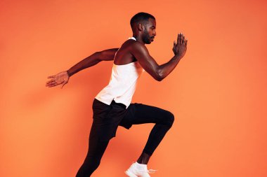 Stüdyoda turuncu arka planda koşan bir erkek koşucunun görüntüsü.