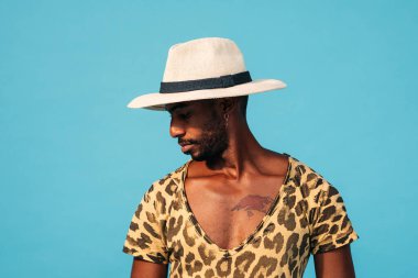 Mavi arka plana bakan şapkalı şık bir adamın portresi.