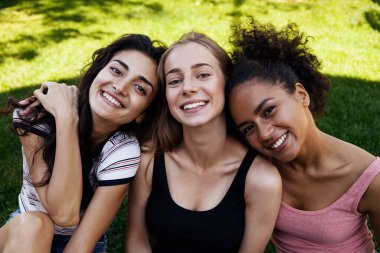 Üç genç kadın parkta oturuyor ve sarılıyorlar.