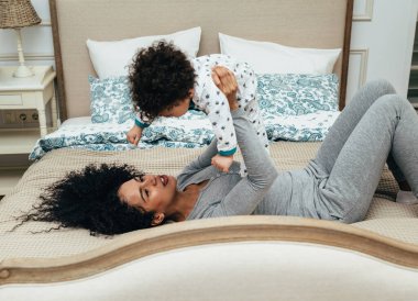 Young beautiful mother playing with her baby on a bed