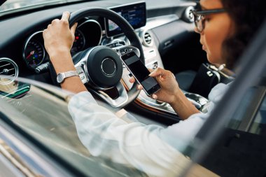 Unrecognizable woman using smartphone while sitting in car.	