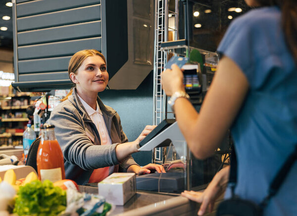 Smiling female cashier accepting payment from customer, entering data into terminal