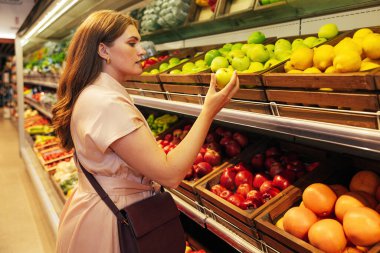 Bir markette dururken elinde yeşil elma tutan kadın müşteri.