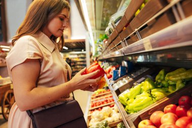 İki dolmalık biber alıp karşılaştıran kadın müşteri. 