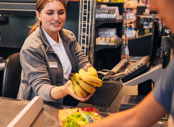 Cheerful female working as a cashier in a grocery store, holding bananas