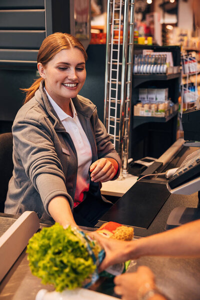Smiling woman working as a cashier in grocery store sitting at the counter 