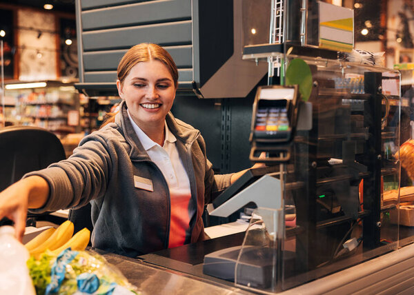 Young smiling woman working as a cashier in a grocery store, sitting at the counter