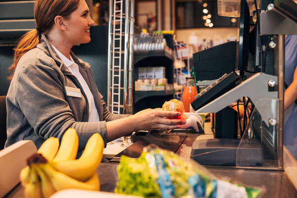 Side view of a female smiling cashier using barcode scanner on a pack on spaghetti, focus on her hands
