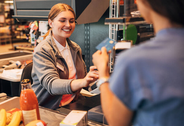 Smiling cashier in a grocery store receiving payment from a customer using pos terminal 