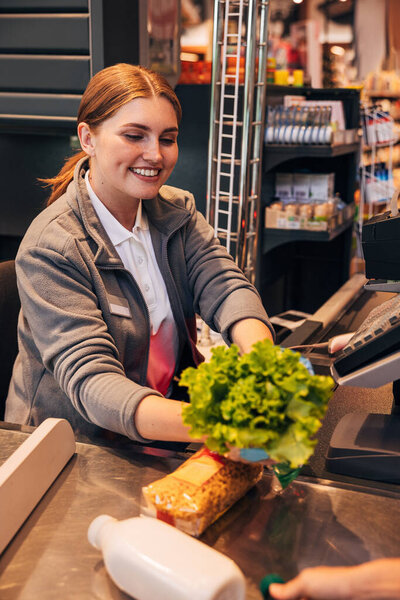 Cheerful woman cashier holding a salad while sitting at counter in grocery store 