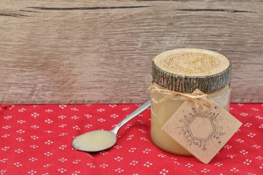 Kağıtlı bal kavanozu ve kırmızı masa örtüsünün üstünde bal.