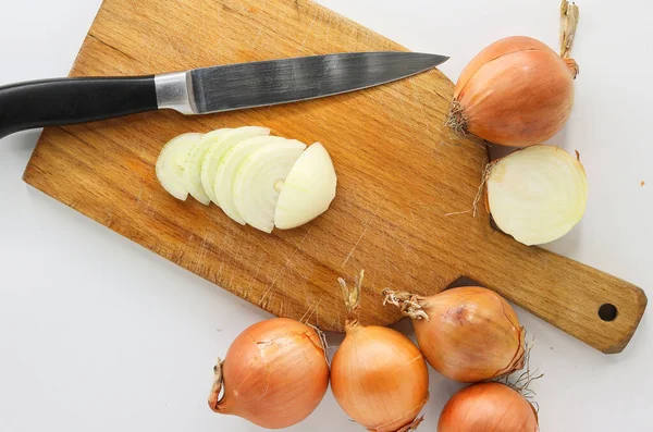 A cutting board and a knife with chopped onion and whole, unpeeled onions