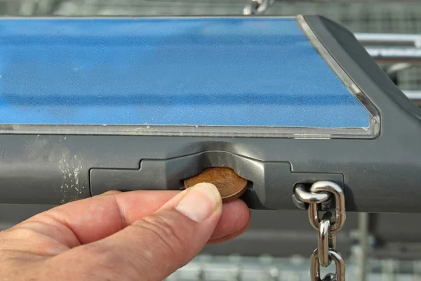 Close-up of a customer\'s hand inserting a coin into a shopping cart on the handle of the trolley instead of writing text