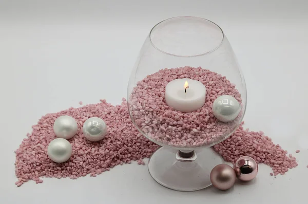 Christmas candle holder made of candle in a glass, decorative pink sand and small Christmas balls