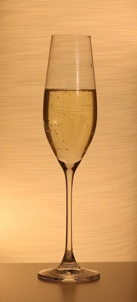 One glass with champagne or sparkling wine on a lit background