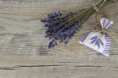 Bir buket kurutulmuş lavanta ve ahşap bir zeminde kurutulmuş otla dolu bir bez poşet.