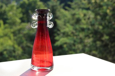 Akşamları bahçedeki bir masanın üstünde berrak ve kırmızı camdan yapılmış küçük cam bir vazo.