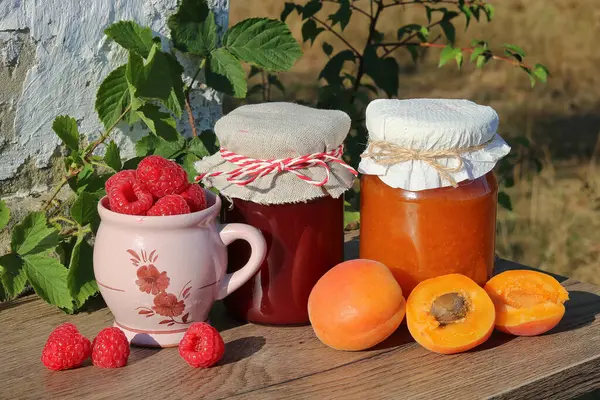 stock image Raspberries, apricots and marmalades made from them on a table in the garden of a country cottage