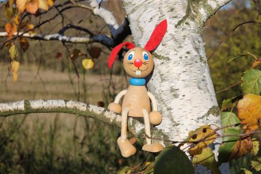 Geleneksel ahşap oyuncak tavşancık sonbahar doğasında bir huş ağacının dalına tünemişti.