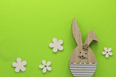 Yeşil arka planda bir tavşan ve çiçekler olan Paskalya kartı.