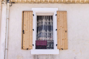 Saintes-Maries-de-la-Mer, Bouches-du-Rhone, Provence-Alpes-Cote d'Azur, France. Window with wooden shutters and lace curtains in Saintes-Maries-de-la-Mer.