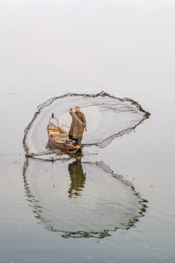 Dal Lake, Srinagar, Jammu ve Kashmir, Hindistan. 26 Ekim 2022. Balıkçı ağını Dal Gölü 'ndeki bir tekneden atıyor..