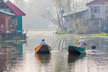 Dal Gölü, Rainawari, Srinagar, Jammu ve Kaşmir, Hindistan. 26 Ekim 2022. Erkekler geleneksel teknelerle Dal Gölü 'ndeki evlerin önünden geçiyor..
