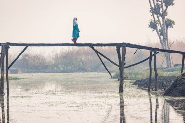 Dal Gölü, Rainawari, Srinagar, Jammu ve Kaşmir, Hindistan. 26 Ekim 2022. Dal Gölü 'nde bir yaya köprüsünden geçen bir kadın..