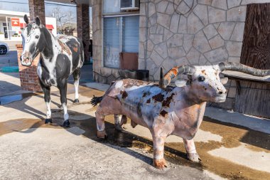 Yoakum, Teksas, Birleşik Devletler. 17 Mart 2022. Uzun boynuzlu bir sığırın metal halk sanatı heykeli ve kaldırımda bir at mankeni.