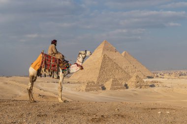 Giza Piramit Kompleksi, Al Ahram, Giza, Mısır. 21 Şubat 2023. Büyük Piramit olarak da bilinen Menkaure, Khafre ve Khufu piramitlerinin önündeki devenin üzerindeki adam..