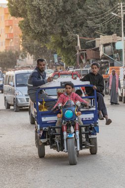 Al Wahat Al Baharia, Giza, Mısır. 20 Şubat 2023. Mısır 'ın batısındaki Bahariya vahasında üç tekerlekli bisiklet süren bir çocuk ev eşyaları taşıyor..