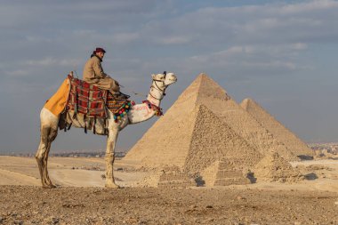 Giza Piramit Kompleksi, Al Ahram, Giza, Mısır. 21 Şubat 2023. Büyük Piramit olarak da bilinen Menkaure, Khafre ve Khufu piramitlerinin önündeki devenin üzerindeki adam..