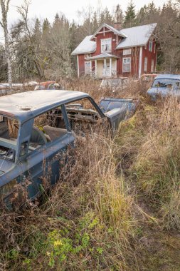 Piçler, Varmland, İsveç. 3 Kasım 2024. Terk edilmiş ev ve hurda arabalar Bastnas araba mezarlığında..