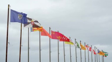 Otantik bayraklar yavaş çekimde İspanya Krallığı 'nın özerk topluluklarının direkleri bulutlu bir gökyüzünde güçlü bir rüzgarla dalgalanırken. Endülüs, Aragon, Asturias, Islas Baleares