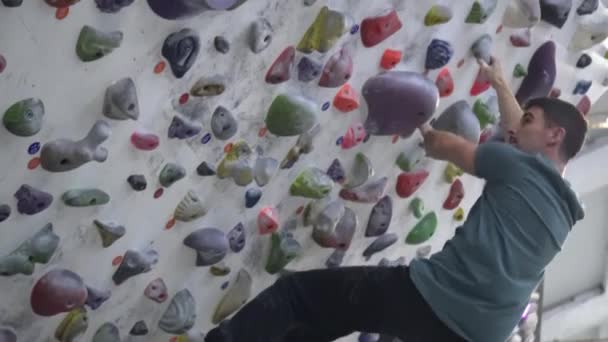 登山ジムの中の人工的な登山壁に登る男の側面ショット スポーツ活動と健康的な生活 高品質の4K映像 — ストック動画