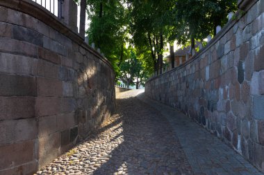 Kaunas, Litvanya. 30 Haziran 2024. Eğri duvarlar arasındaki taş asfalt yol, güneş ışığına çıkıyor.