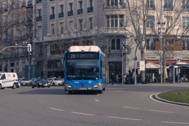 Madrid, İspanya. 15 Şubat 2025. Arka plandaki dolambaçlı ve tarihi binalarda mavi bir acil yardım Madrid otobüsü.
